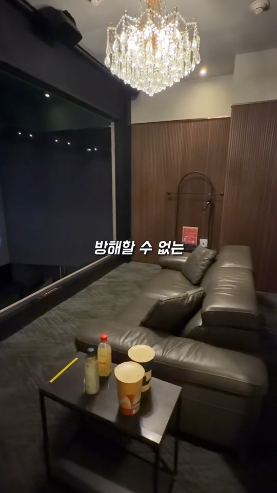 스크린 옆 샹들리에와 소파, 테이블이 놓인 CGV 프라이빗 박스 내부